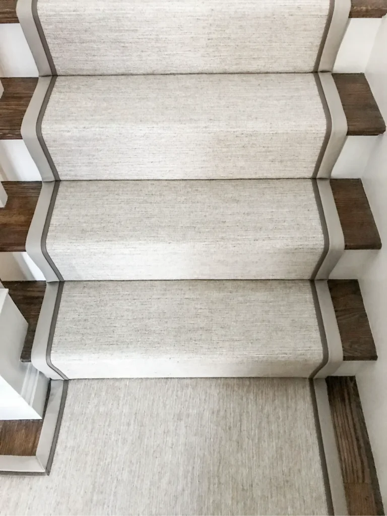 Cream herringbone stair runner with grey border and metal rods.