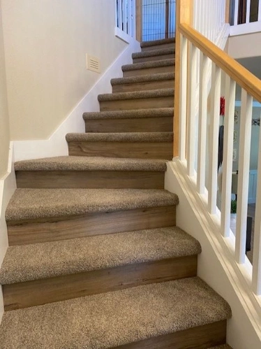 Light brown plush carpet on wooden stairs with white and wood railing.