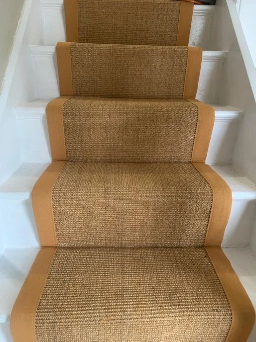 Premium natural sisal stair carpet with border piping installed on a white staircase, a popular home flooring choice in Dubai.