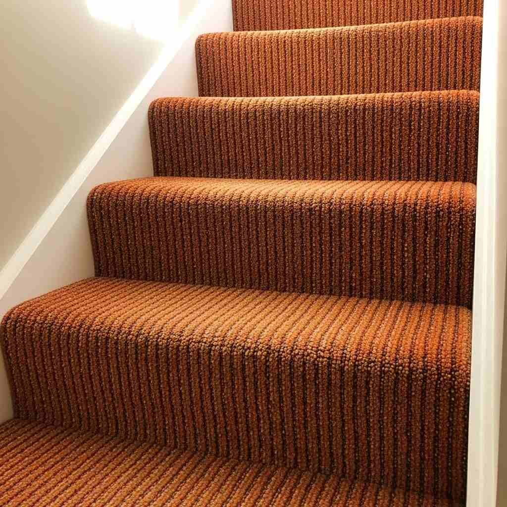 Staircase with orange textured carpet runner and brown shoes placed on the steps in a cozy home interior