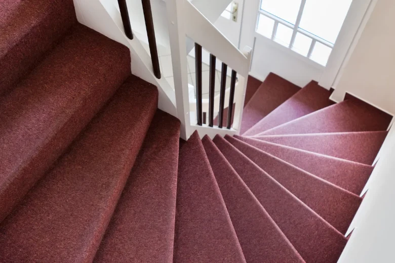Winding stairs covered in deep maroon carpet.