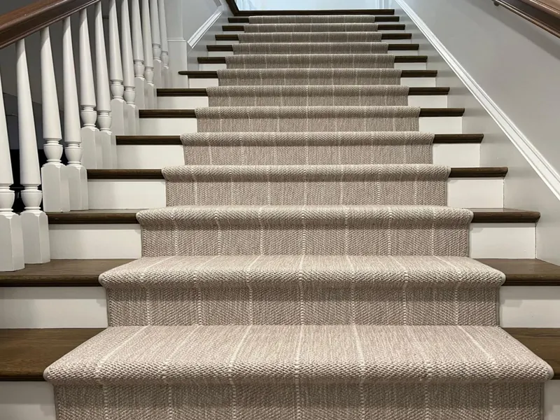 beige wool carpet runner with a subtle white pinstripe pattern covers the center of the stairs