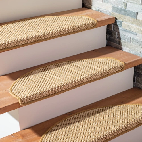 sisal stair treads with a textured weave and finished edges, installed on modern light-wood stairs with white risers next to a grey stone wall.