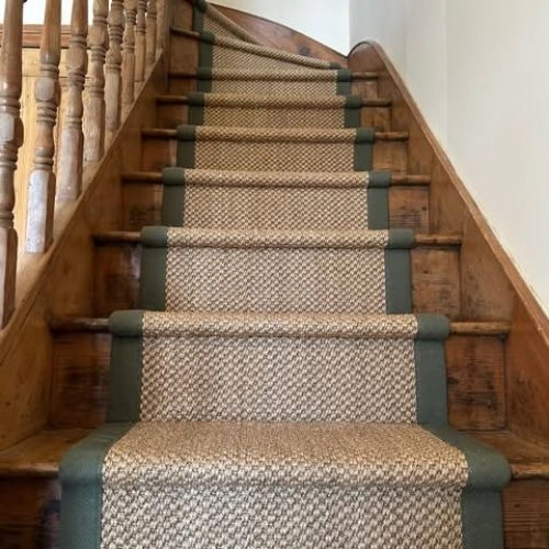 wooden stairs featuring a textured, light brown sisal carpet runner with a dark green fabric border.