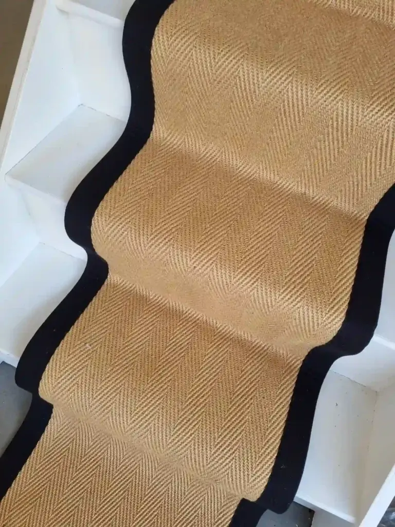 Natural herringbone sisal stair runner with a black border on white wooden stairs.