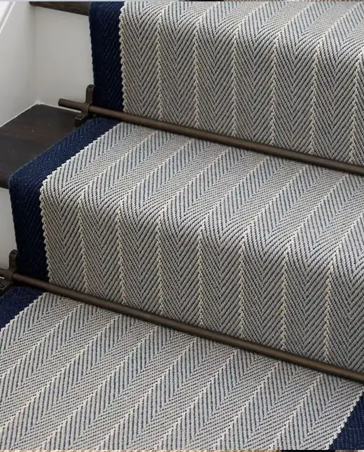 Blue and grey herringbone patterned stair runner with dark border trim and metallic stair rods fitted on wooden steps for Herringbone Stair Runners Dubai.