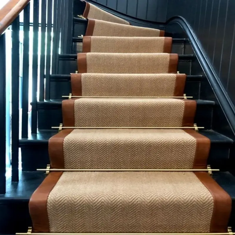 Dark wooden staircase with a beige herringbone stair runner, brown leather trim, and brass stair rods.