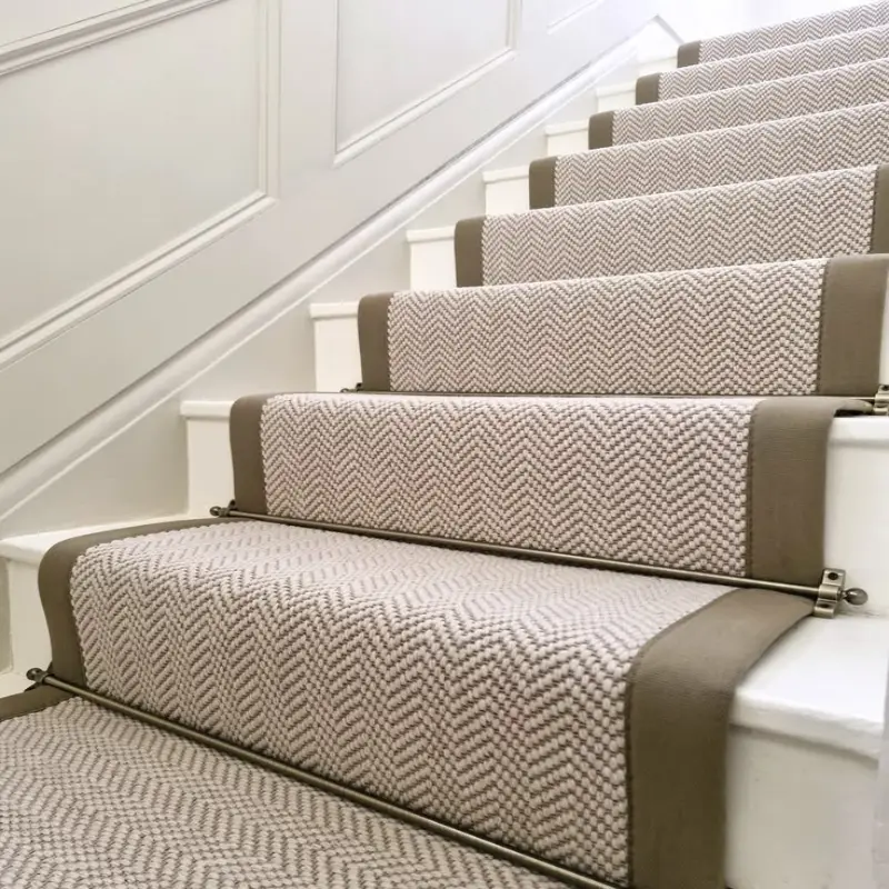 Herringbone Stair Carpet runner in beige with taupe border binding and brass stair rods on white steps.