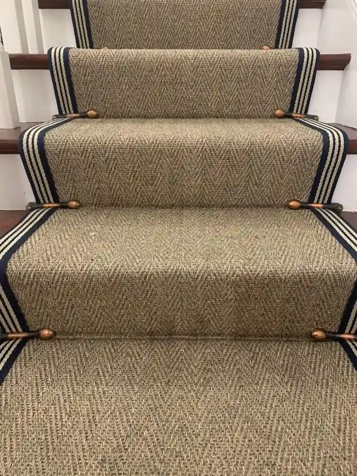 Natural woven sisal stair carpet runner featuring bold navy blue striped border binding and decorative stair rods for Sisal Stair Runners Dubai.